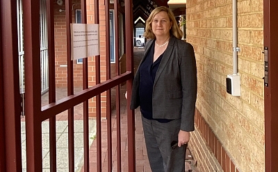 Image of a well-dressed woman standing in an outdoor corridor holding open a gate as if she is inviting us inside