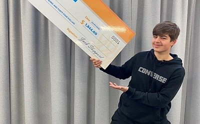 A young person enthusiastically holds up a large-scale cheque addressed from 'jack's creative kitchen' to St Bart's