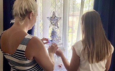 Two people put the finishing touches on a Christmas tree that sits in the front window of a house