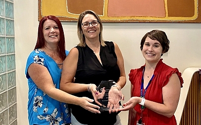 Three people joyously hold a clear glass award together