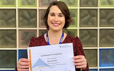 Sara Zanella wearing a red patterned dress holds an award up that says 'certificate of completion'