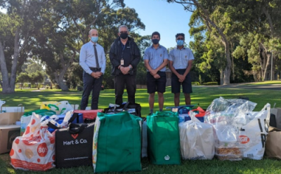 In the foreground of the image, there is a large volume of shopping bags all filled up. The background is a park, with four people standing over the bags