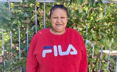 Lynette standing in front of a fence with a large green plant growing behind it