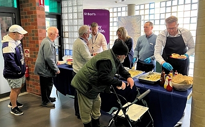 People gather to serve and eat food at a long table with large trays on it